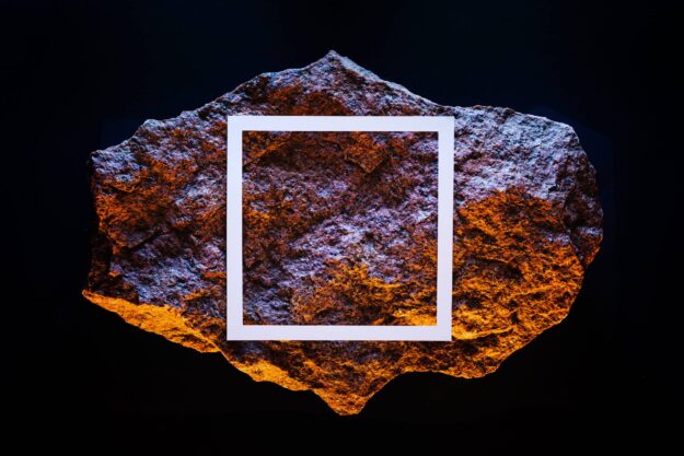 A yellow meteorite in a dark space with a white frame and a neon fluorescent light.